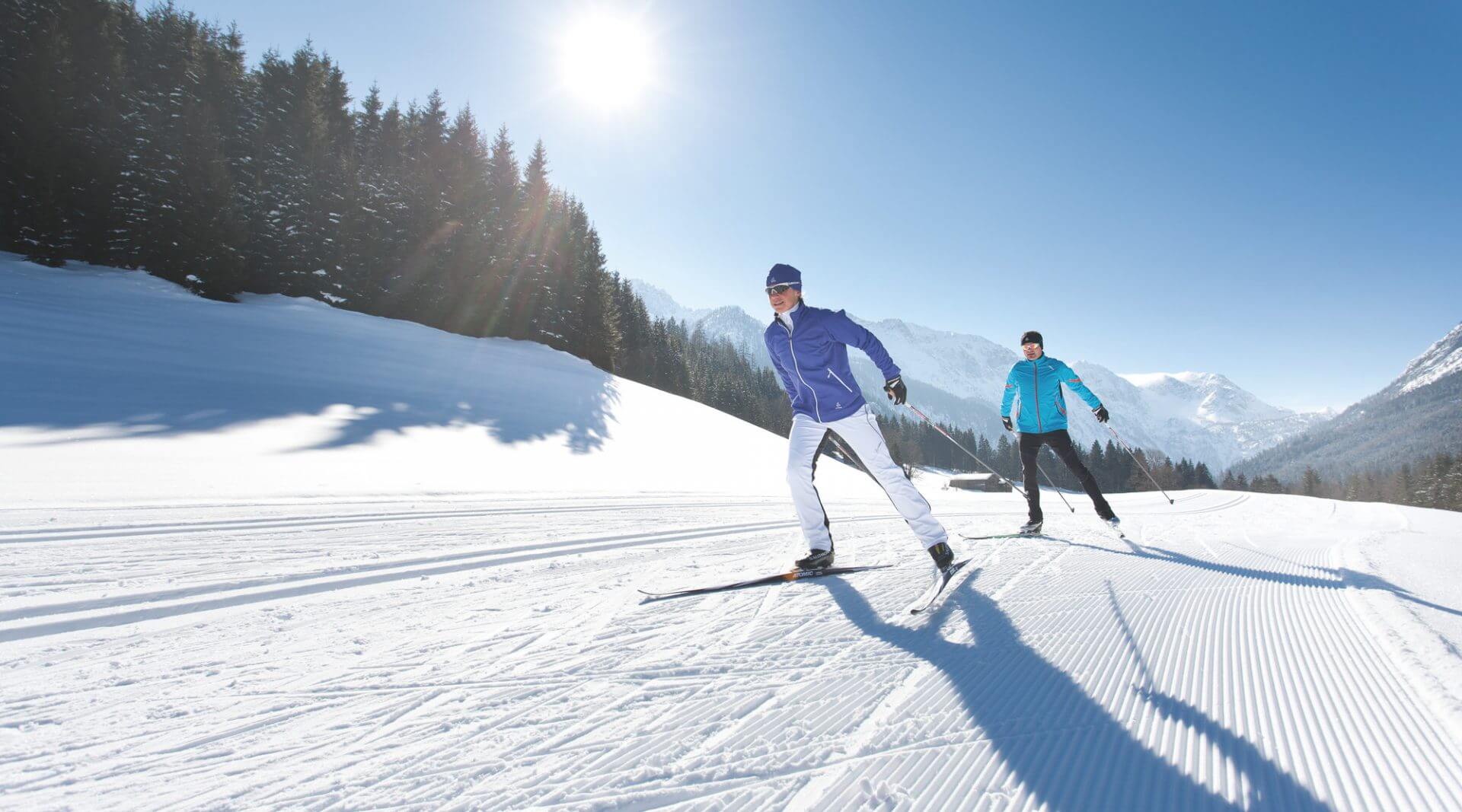 Zwei Längläufer beim Skating auf der Piste im Sonnenschein.